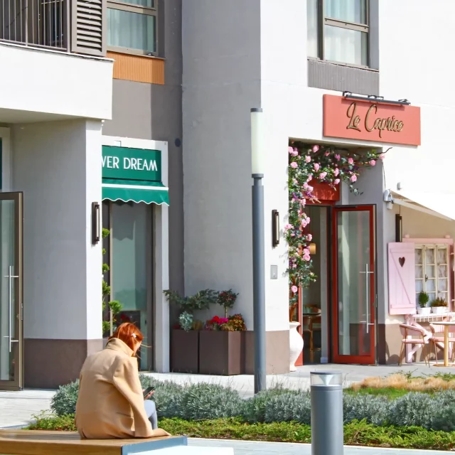 A girl is sitting in front of the Flower Dream flower shop and pastry shop Le Caprice.